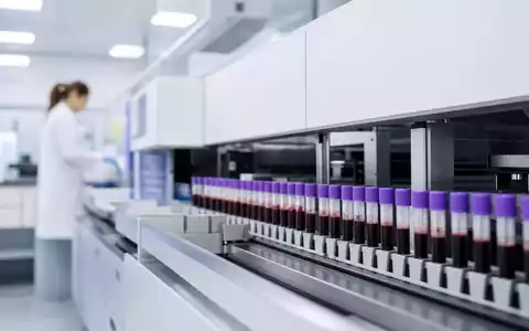 Quest Diagnostics US74834L1008 zeigt automatisierten Laboranalysator mit Blutproben in modernem Diagnostiklabor fotorealistisch dargestellt - Foto: THN