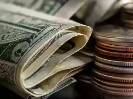 Raymond James Financial US7547301090 zeigt eine Makroaufnahme gefalteter Dollarnoten und gestapelter Münzen - Foto: THN