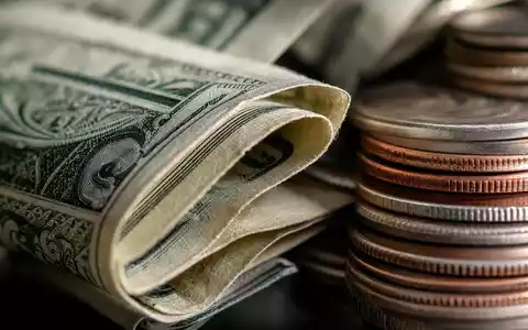 Raymond James Financial US7547301090 zeigt eine Makroaufnahme gefalteter Dollarnoten und gestapelter Münzen - Foto: THN