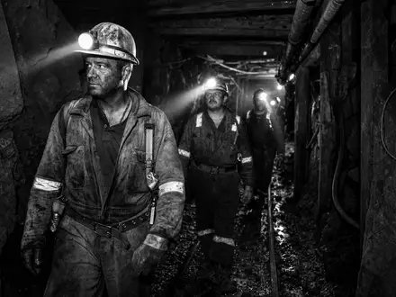 Anglo American plc GB00B1XZS820 dokumentiert Bergleute mit Helmlampen in einem dunklen Untertage-Tunnel schwarzweiß - Foto: THN