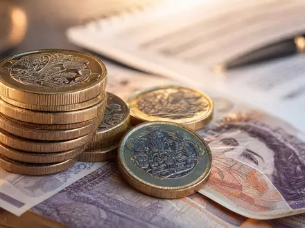 Just Group plc GB00BYV8MN78 fokussiert Makroaufnahme britischer Münzen und Banknoten neben Rentendokument - Foto: THN