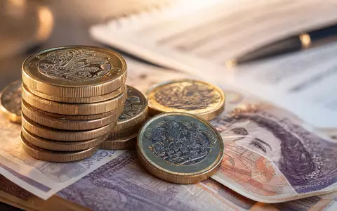 Just Group plc GB00BYV8MN78 fokussiert Makroaufnahme britischer Münzen und Banknoten neben Rentendokument - Foto: THN