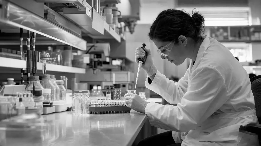 Schwarzweiß-Reportagefoto einer Laborantin bei der Arbeit mit Pipette und Probenröhrchen