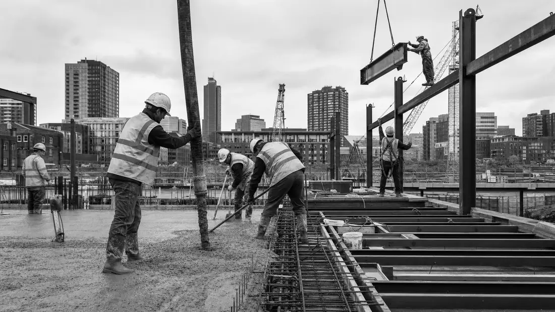Schwarzweiß Reportagefoto von Bauarbeitern auf Baustelle mit Stahlträgern