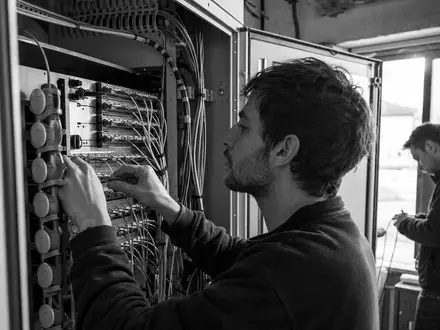 Schwarzweiße Reportage-Fotografie zeigt Techniker bei Glasfaserarbeiten, dokumentiert Tele2 AB, ISIN SE0005190238, im Telekombereich - Foto: THN