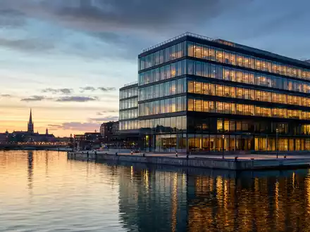 Kinnevik AB (ISIN SE0015810247) zeigt modernes BĂŒrogebĂ€ude am Wasser, symbolisch fĂŒr schwedische Investment-Holding bei DĂ€mmerung - Foto: THN