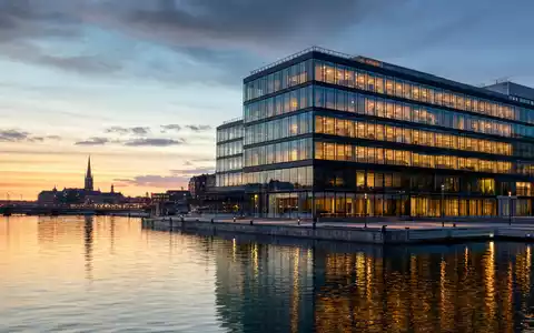 Kinnevik AB (ISIN SE0015810247) zeigt modernes Bürogebäude am Wasser, symbolisch für schwedische Investment-Holding bei Dämmerung - Foto: THN