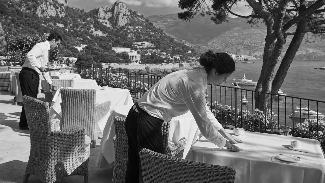 Schwarz-Weiß-Reportagefoto von Hotelpersonal beim Eindecken einer Terrasse