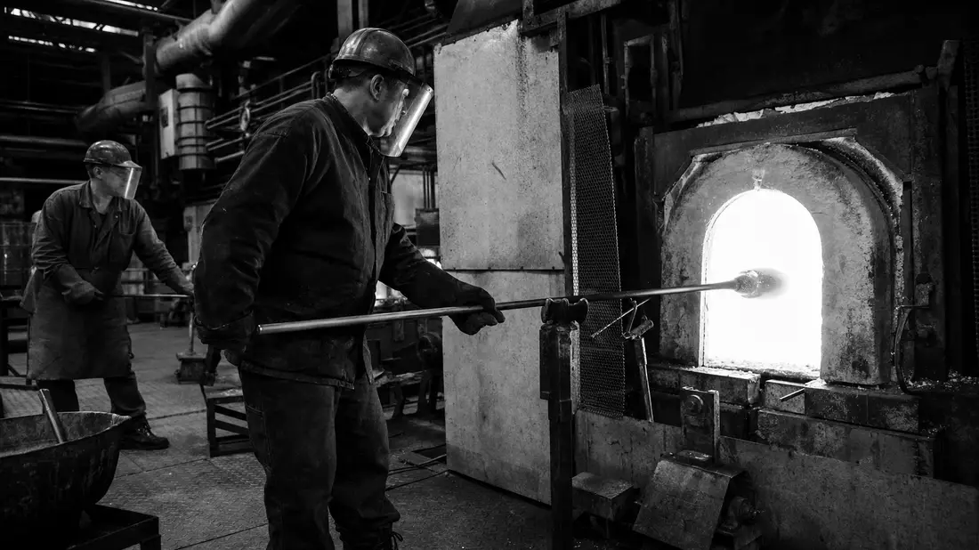Schwarzweiß-Dokumentarfoto von Arbeitern an einer Glasschmelzofen-Produktionslinie