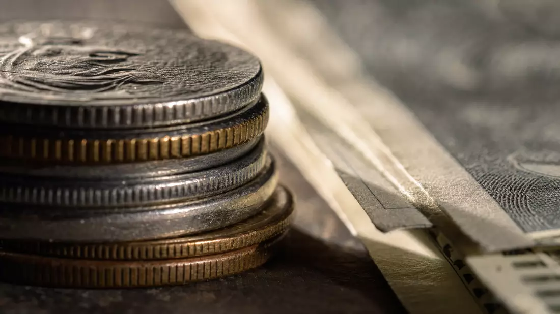 Makroaufnahme von gestapelten Münzen und Banknotenkanten im Streiflicht