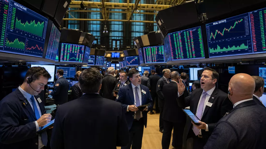 Trading-Floor mit Händlern vor Bildschirmen, die Healthcare- und Immobilien-Charts zeigen