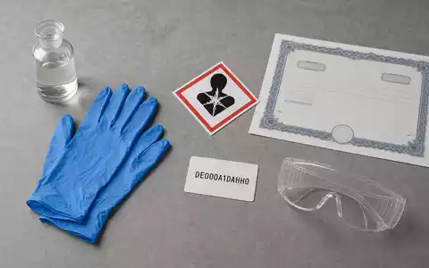 Sorgfältiges Flatlay mit Schutzhandschuhen und Gefahrgut-Symbolen zeigt die Chemiedistribution von Brenntag SE neben ISIN DE000A1DAHH0 - Foto: THN