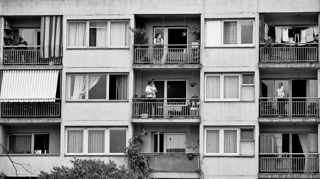 Schwarz-Weiß-Reportagefoto einer Wohnhausfassade mit Bewohnern auf Balkonen