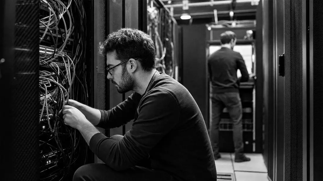 Schwarzweiß-Reportagefoto von IT-Technikern bei Kabelarbeiten im Netzwerkraum