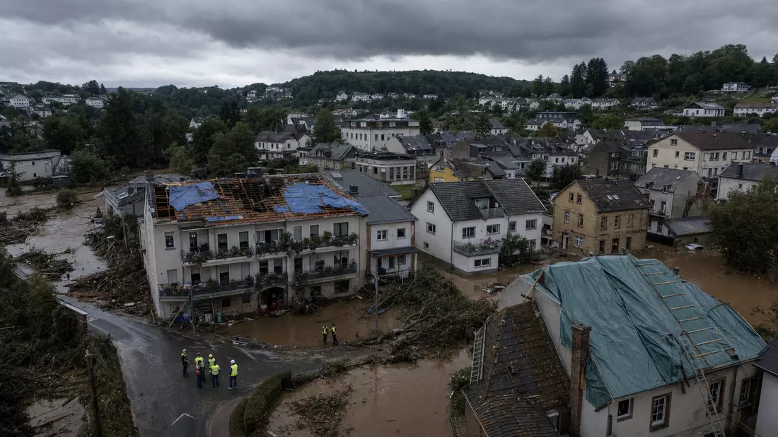 Überflutete Straße mit beschädigten Häusern nach einer Sturmflut, Einsatzkräfte inspizieren die Schäden