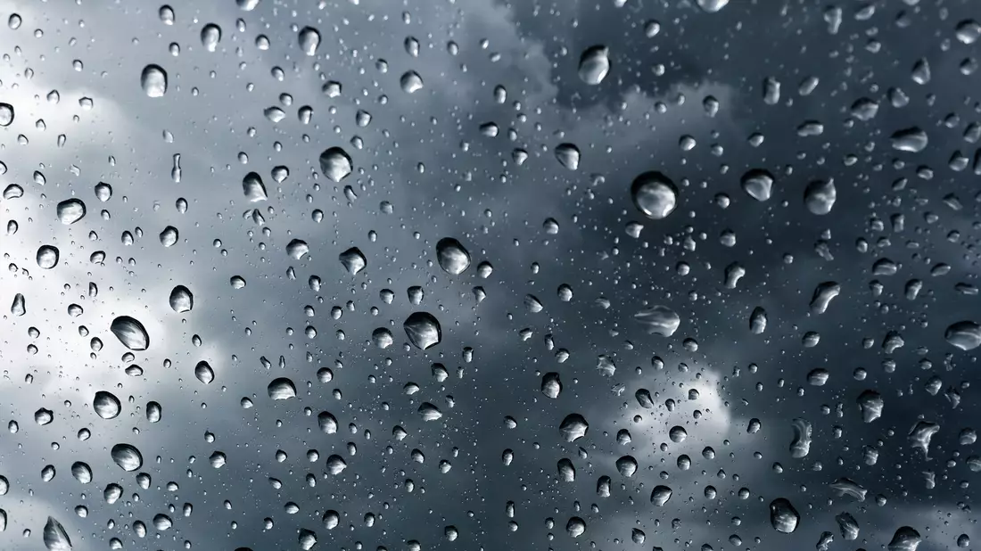 Makroaufnahme von Regentropfen auf Glas mit unscharfen Sturmwolken im Hintergrund