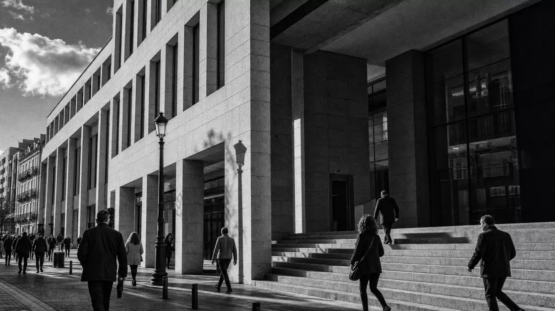 Dokumentarische Schwarzweißaufnahme eines modernen Bankgebäudes mit Passanten auf der Straße