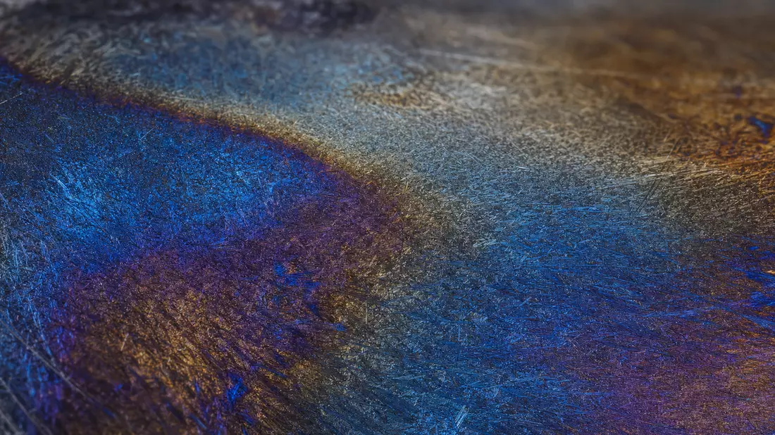 Extreme Makroaufnahme einer Metalloberfläche mit blauen und violetten Anlassfarben nach Wärmebehandlung