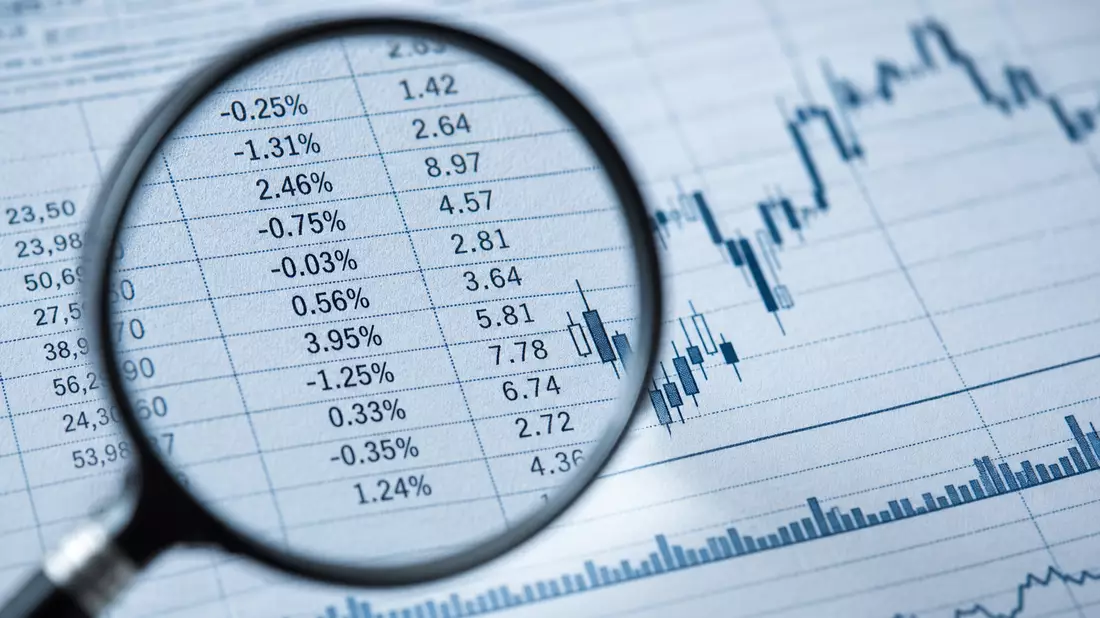 Makrofoto einer Lupe über Prozentzahlen und Candlestick-Charts auf Papier