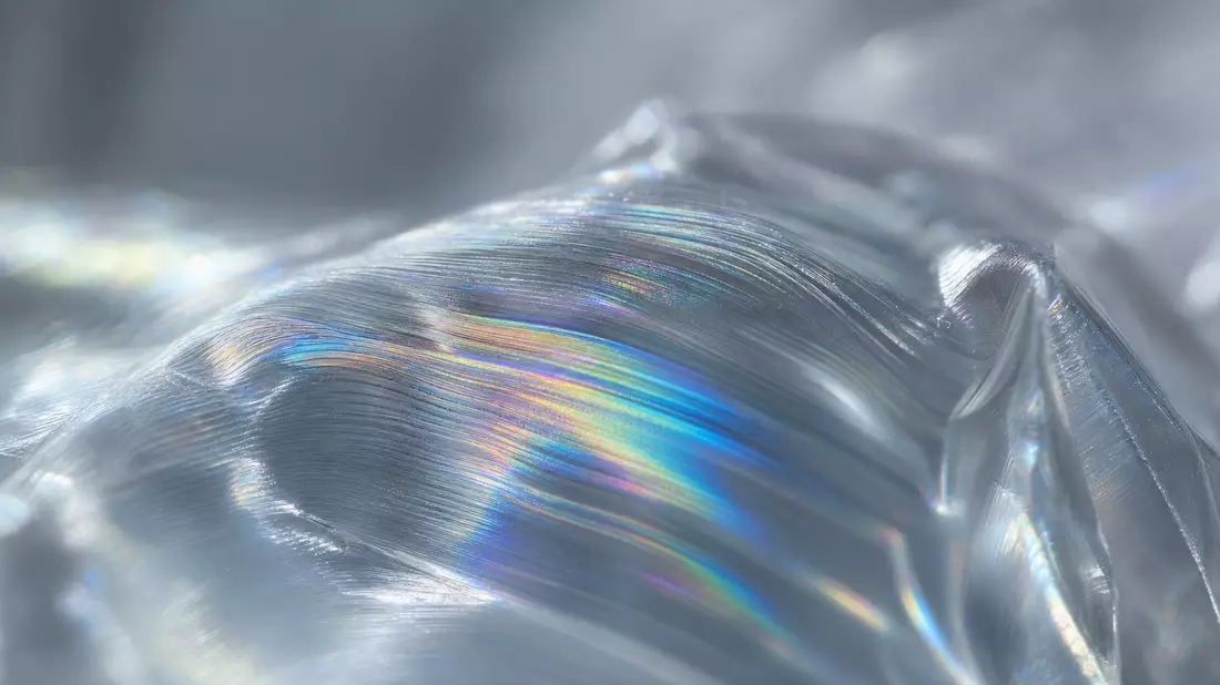 Amcor plc JE00BJ1F6598 macro close-up of iridescent holographic polymer film with rainbow light interference