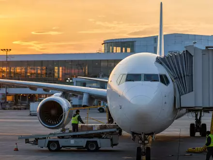American Airlines Group Aktie US02376R1023 fotorealistisches weißes Passagierflugzeug am Gate bei Sonnenuntergang mit Bodenpersonal - Foto: THN