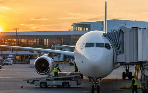 American Airlines Group Aktie US02376R1023 fotorealistisches weiĂes Passagierflugzeug am Gate bei Sonnenuntergang mit Bodenpersonal - Foto: THN