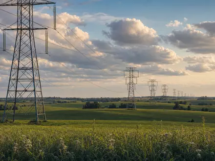 American Electric Power US0255371017 Hochspannungsmasten über grünen Ohio-Feldern bei goldenem Abendlicht mit dramatischen Wolken - Foto: THN