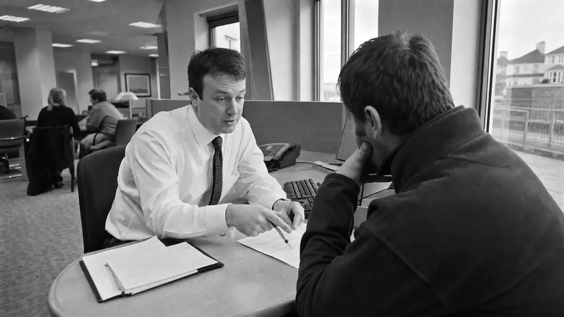 Schwarzweiß-Reportagefoto: Bankberater bespricht Hypothekenunterlagen mit Kunde