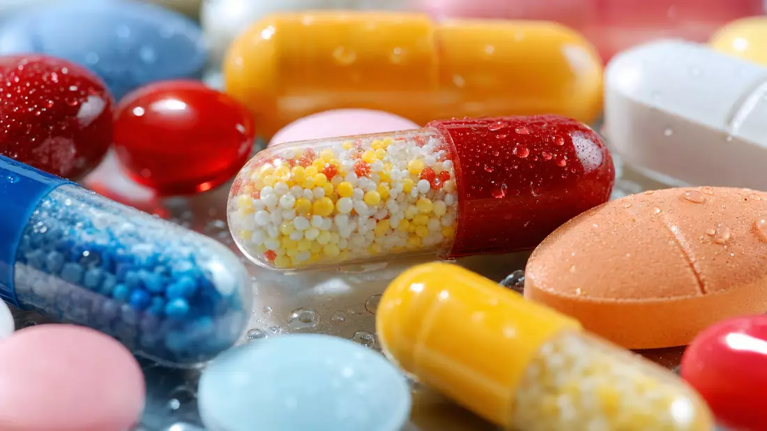Extreme Nahaufnahme bunter Tabletten und Kapseln mit glänzender Oberfläche und Wassertropfen