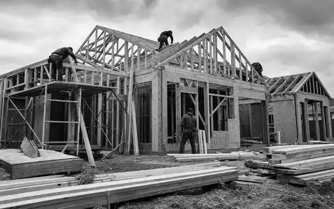 PulteGroup Inc. US7458671010 dokumentiert eine Schwarzweiß-Baustelle mit Holzrahmenkonstruktion und mehreren Bauarbeitern am neuen Einfamilienhaus - Foto: THN