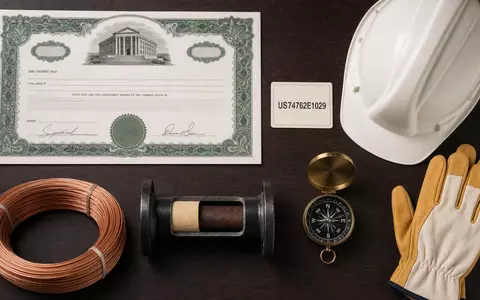 Quanta Services Inc. (ISIN US74762E1029) Investment-Flatlay zeigt Aktienzertifikat, ISIN-Karte und Bauarbeiter-Utensilien arrangiert - Foto: THN