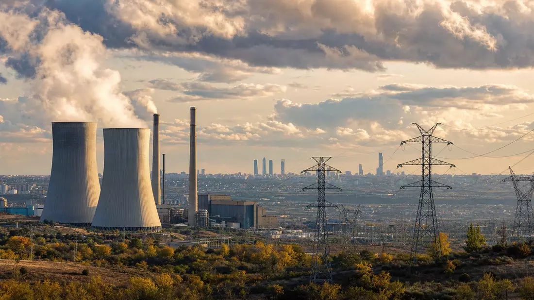 Fotorealistisches Kraftwerk mit Kühltürmen und Strommasten vor Madrider Skyline