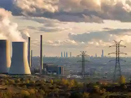 Endesa S.A. ES0130670112 zeigt Kraftwerk mit Kühltürmen und Hochspannungsmasten vor Madrider Skyline im Abendlicht - Foto: THN