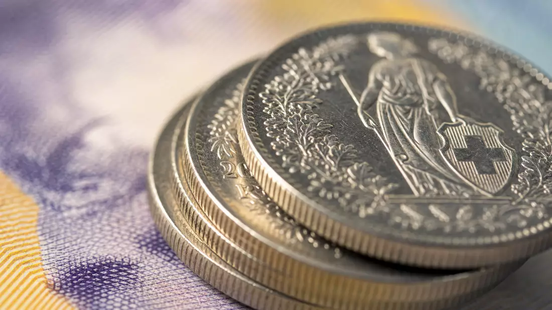 Makroaufnahme glänzender Schweizer Münzen auf Banknotenhintergrund
