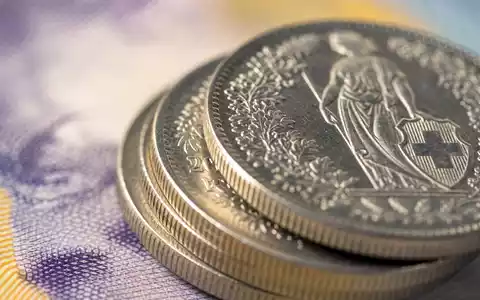 Julius BĂ€r Gruppe AG (ISIN CH0102484968) veranschaulicht Makroaufnahme glĂ€nzender Schweizer MĂŒnzen vor Banknotenhintergrund - Foto: THN