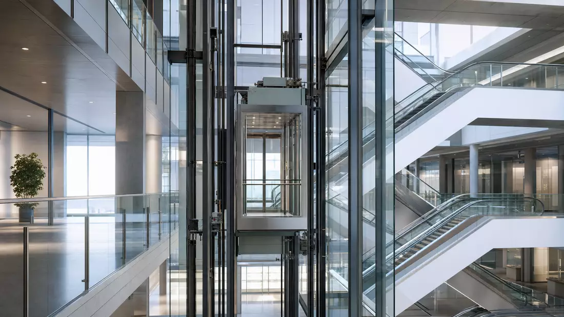 Glasaufzug mit Rolltreppen in hellem Atrium eines modernen Bürogebäudes