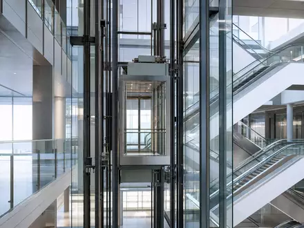 Schindler Holding AG (ISIN CH0024638196) zeigt gläsernen Aufzugschacht mit Rolltreppen in modernem Bürogebäude-Atrium - Foto: THN