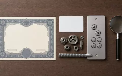 Schindler Holding AG (ISIN CH0024638196) zeigt Flatlay mit Aktienzertifikat, ISIN-Karte, Zahnrädern und Aufzug-Bedienfeld auf Holztisch - Foto: THN