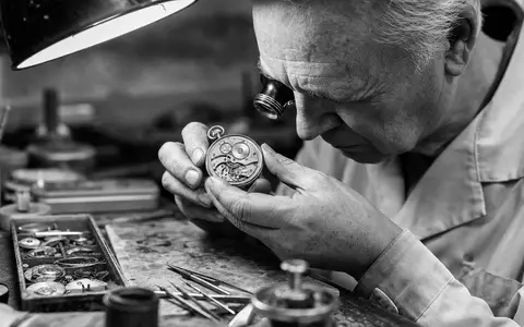 Dokumentarische Schwarzweiß-Reportage illustriert The Swatch Group AG (CH0012255151), Uhrmacher prüft mechanisches Taschenuhrwerk konzentriert - Foto: THN