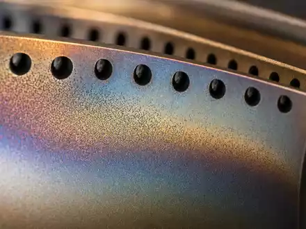 Rolls-Royce Holdings plc (GB00B63H8491): Makroaufnahme zeigt Turbinenschaufel-Oberfläche mit feinen Kühlbohrungen und metallischem Farbschimmer - Foto: THN