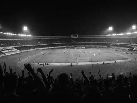 Schwarzweiß-Reportage zeigt Sportstadion bei Nacht, passend zu Flutter Entertainment plc ISIN IE00BWT6H894 Wettgeschäft - Foto: THN