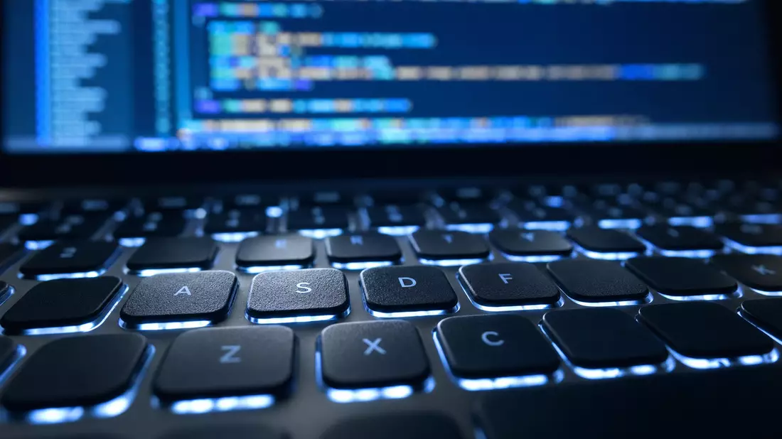 Extreme Nahaufnahme einer beleuchteten Laptop-Tastatur mit unscharfem Quellcode dahinter