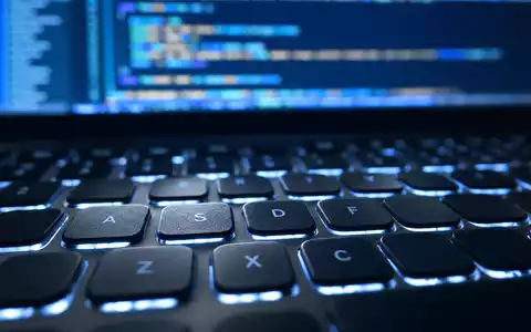 Paylocity Holding US70436Y1038 zeigt Makroaufnahme einer beleuchteten Laptop-Tastatur mit unscharfem Quellcode im Hintergrund - Foto: THN