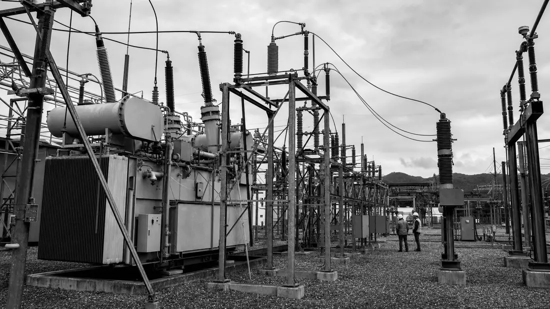 Schwarzweißes Umspannwerk mit Transformatoren und zwei Arbeitern