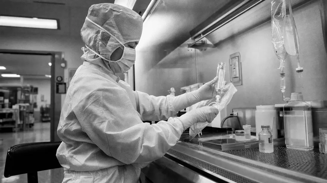 Schwarzweiß-Reportagefoto einer Pharmazeutin bei der Zubereitung einer Infusion im Reinraum