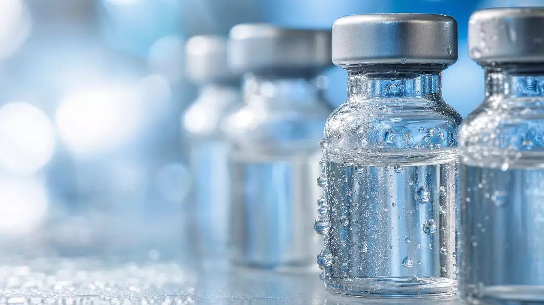Makroaufnahme von klaren Glasfläschchen mit Wassertropfen vor blauem Bokeh-Hintergrund