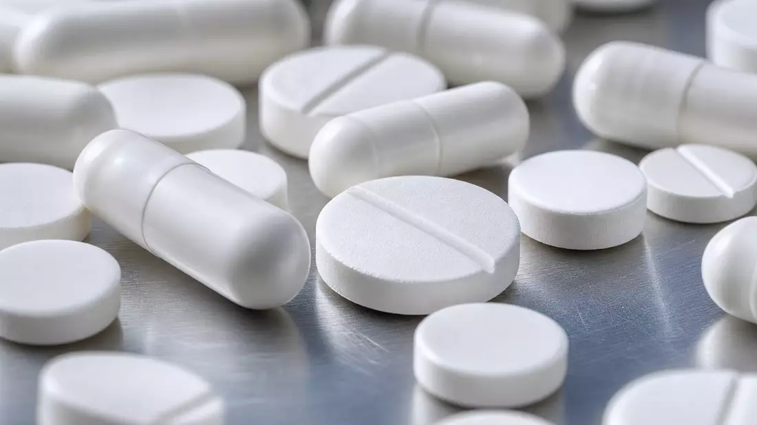 Extreme Nahaufnahme weißer Tabletten und Kapseln auf glänzender Metallfläche