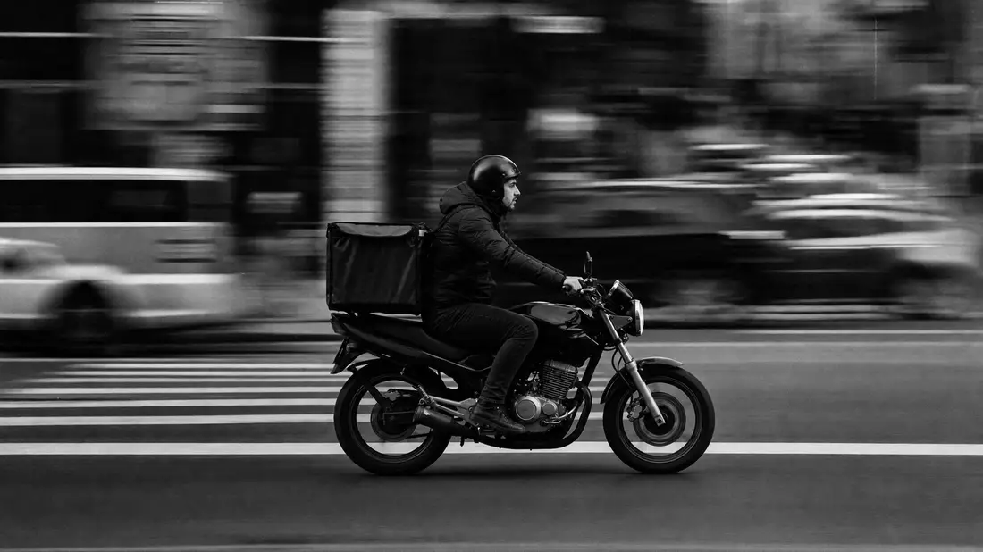 Schwarzweiß-Reportage: Lieferkurier auf Motorrad in Stadtverkehr