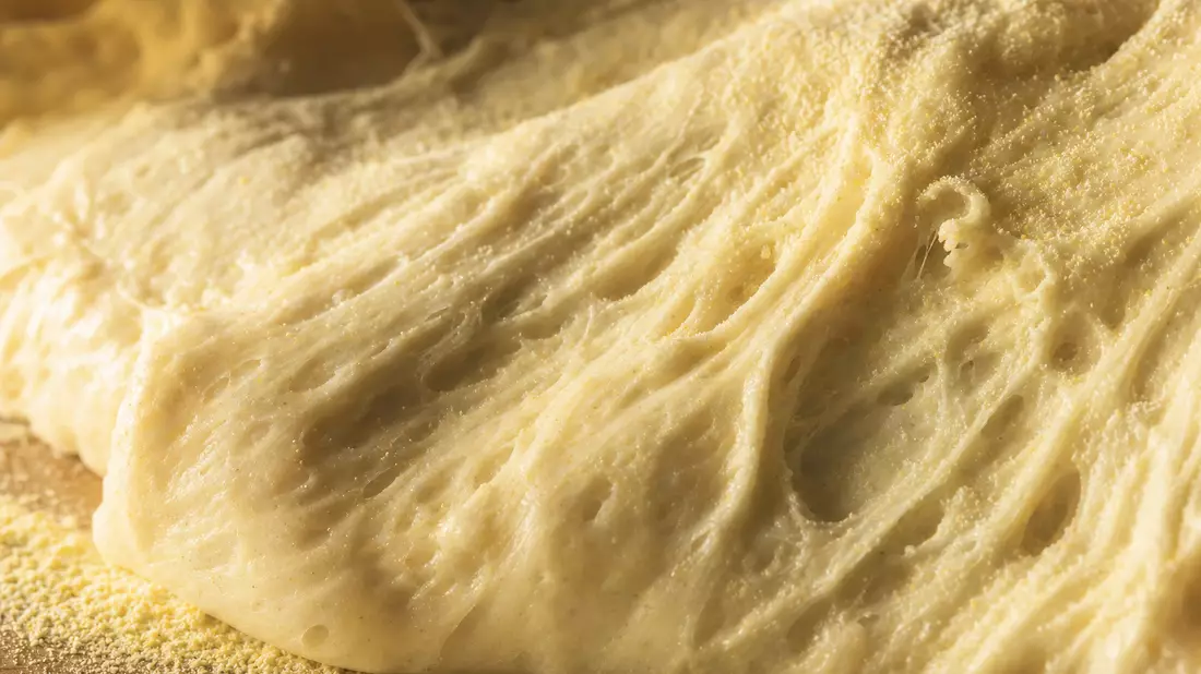 Extreme Nahaufnahme von Pizzateig-Oberfläche mit Luftblasen und Grieß