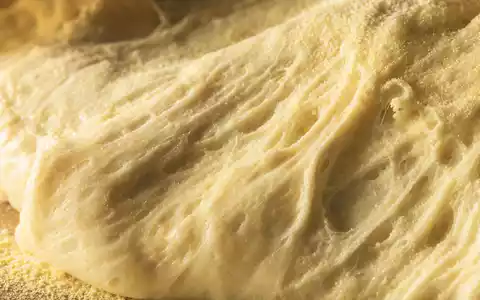 Domino's Pizza US25754A1016 extreme Makroaufnahme von Pizzateig-Oberfläche mit Luftblasen, Grieß und warmem Seitenlicht - Foto: THN